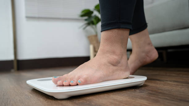 istock Fat diet and scale feet standing on electronic scales for weight control. Measurement instrument in kilogram for a diet control. 1578045584