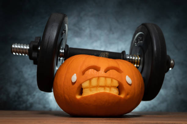 istock Halloween gym concept with carved pumpkin lifting dumbbells. 1578064207