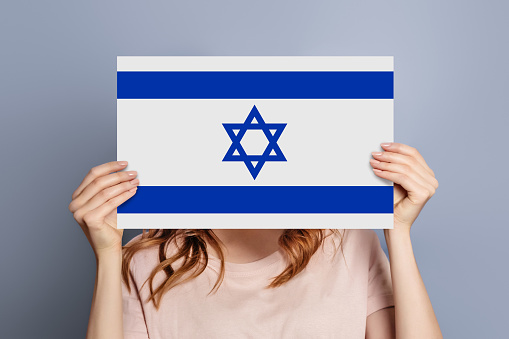 Israel news concept. Female hands holding a round information piece of paper dialog with israel flag isolated over grey studio background