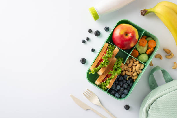 istock Wholesome lunchtime scene from a top-down perspective, showcasing a lunchbox with delightful sandwiches, veggies, fruits and berries on a white isolated background with space for text or promotion 1578094682