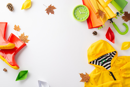 Fun-filled autumn rain concept for children. From above, capture the essence with a top-down photo of a colorful umbrella, rain coat, rubber boots on a white backdrop, ready for text or advertising