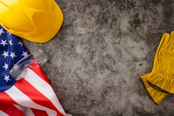 istock Recognizing the invaluable contributions of construction workers on American Labor Day. Above photo of flag, helmet and gloves on grunge textured grey concrete backdrop. Ideal for ads or text 1578103839