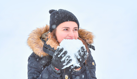 Young girl with eyes closed and smiling in black hat holding snow with her hands