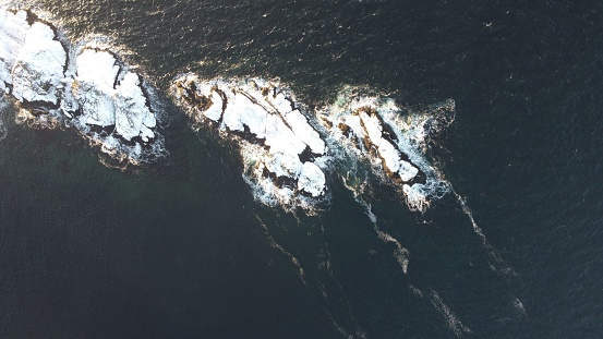An aerial top down view of rugged coastal cliffs with clear blue water below