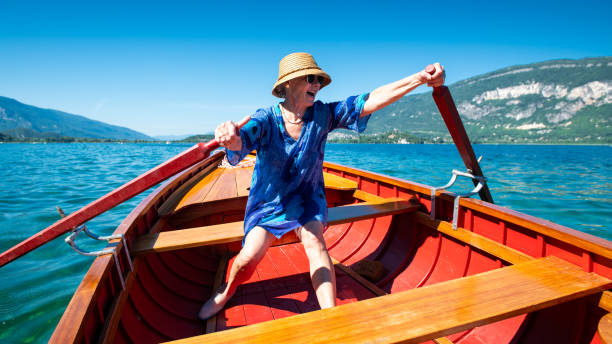 Senior lady with a hat and sunglasses trying to row on a lake with a smile on her face