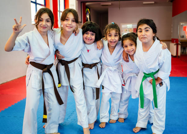 un groupe d’enfants d’âge primaire suit un cours d’arts martiaux. ils sont debout ensemble dans une rangée et sourient en regardant la caméra. - child sport karate education photos et images de collection