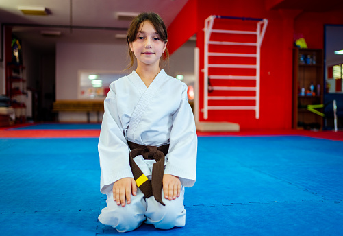 little girl karate student kneeling on exercise mat