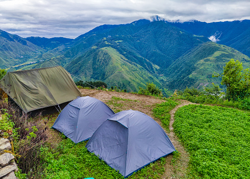 Scenic campground with dome tents and a big living tent, nestled in Nag Tibba's Himalayan region, offering breathtaking mountain peaks and valley views.
