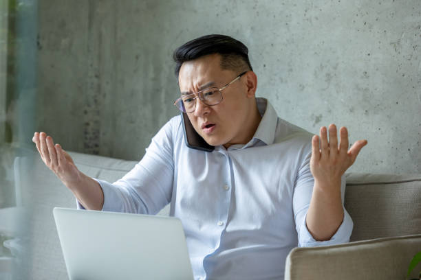 istock Angry stressed man entrepreneur working sitting on sofa working on laptop and talking mobile phone. 1578298080