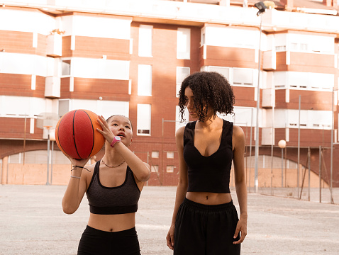 The curly-haired Dominican girl and her Chinese friend play basketball during a summer afternoon.