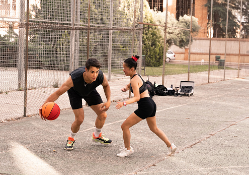 A dark-haired, muscular boy plays basketball with his Chinese friend.