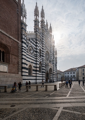 Monza, Italy – September 25, 2022: A crowd of people ambling past the towering Monza Cathedral on a sunny day. Italy.