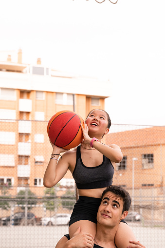 Brown boy lifts Chinese friend onto his shoulders and they play basketball in summer