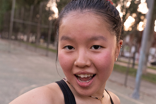 Chinese girl stands on a basketball court and smiles - photos of young people of different races playing sports.