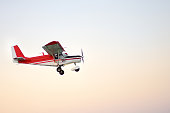 Small ultralight airplane with overhead wing and single propeller flying in sky. Such aircraft are used for recreational, sport and flight training.