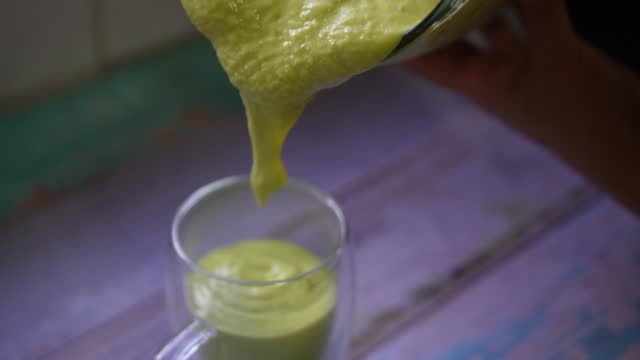 Slow motion video showing a demonstration of pouring an avocado smoothie into a drinking glass.