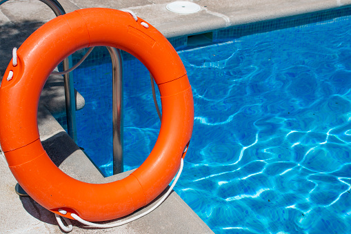 Orange rescue float resting on the steel ladder of a swimming pool