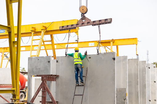 Reinforced concrete structures. Man construction worker control large crane for placing precast concrete panels at Heavy Industry Manufacturing Factory