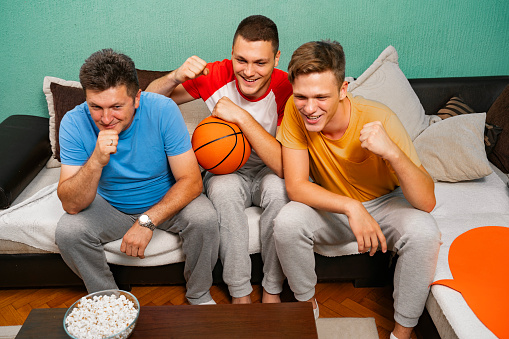 Family, father and two sons, watching basketball at home on tv, cheering and having fun