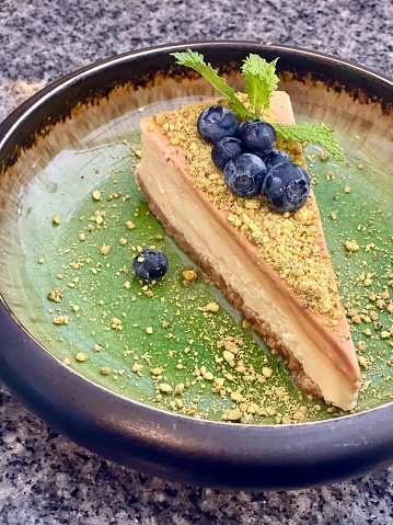 Cheesecake with pistachios and fruit on green plate