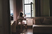 Back view of beautiful woman with cup of coffee in a transparent nightgown sitting on the armchair near open window.