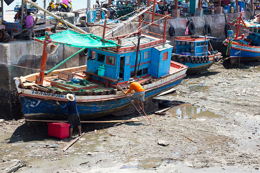 Thai fisher men at boat during low tide captured in harbor of island Ko Sichang. One man is stepping up ladder. Ko Sichang is small island in province of Chonburi close to Siracha