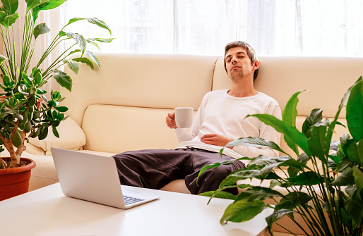 Young man with coffee cup relaxing  on sofa. Coffee break on remote work from home concept.