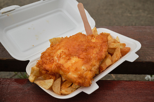 Carton of traditional Fish and Chips on a wet park bench in Newquay, Cornwall between the showers on a rainy June day.