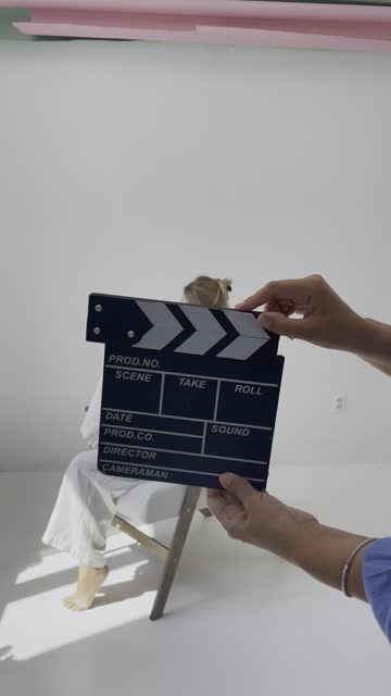 Young woman actress sitting in armchair. Using movie clapperboard audition in white studio. Vertical 4k footage