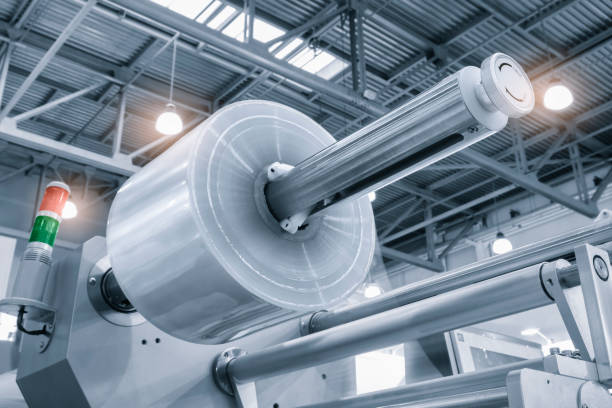 istock Automatic industrial machine for plastic packaging with light effect of products and food. shaft of an automated packaging line with plastic film in a light blue scene. product packaging concept 1578558923