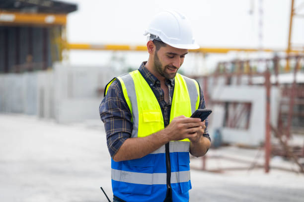istock building and construction worker using mobile phone, Hiapanic latin male wearing safety hard hat helmet standing with arms crossed at construction site and looking at camera 1578560821