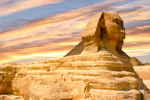 Behold the Egyptian Sphinx's mesmerizing beauty as it stands elegantly against a magnificent sunset in Giza, Egypt. This ancient structure bears the secrets of a long-gone past and beckons you to go on a trip through time and history.