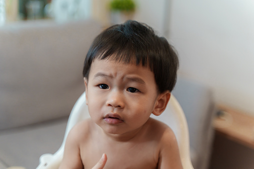 Little cute Asian baby boy with suspicious look and innocence while waiting for his father to cut his hair.