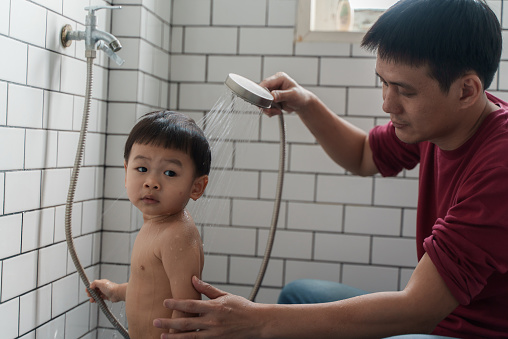 Young Asian father showering his son in bathroom. Cute Asian toddler boy enjoying and relaxing while taking a bath. Family lifestyle parent connection affectionate concept.