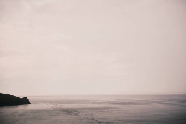 Gloomy rainy views across a calm overcast raining Newquay bay, Cornwall. A group of unrecognisable paddle boarders in the distance.
