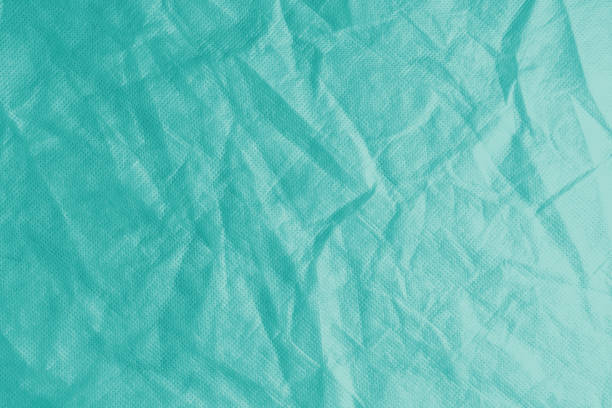 Wrinkled, crumpled turquoise fabric texture background. Wrinkled and creased abstract backdrop of spunbond  textile, wallpaper with copy space, top view.