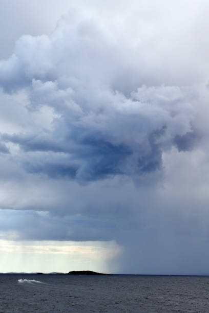 Vertical photo of dark clouds and rain above the horizon at sea.