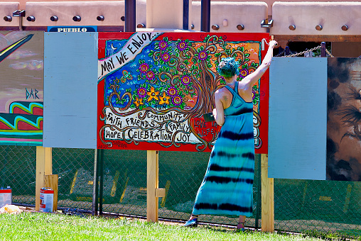 Taos, New Mexico, USA - July 24, 2023: A woman applies water sealant to freshly-painted artwork by artist Julie Terrell that is part of the Paseo Project to beautify Taos Plaza during its renovation by creating a temporary mural with the collaboration of 12 local artists.