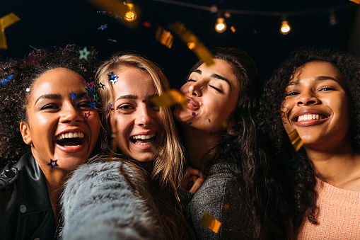 Four laughing girls taking selfie under confetti at night