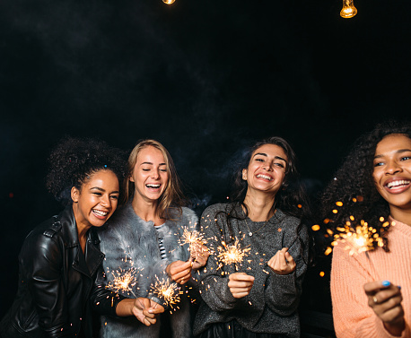 Four happy females with sparklers. Group of diverse female friends celebrating at night.