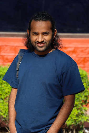Stock photo showing portrait of a casually dressed Indian man standing outdoors.