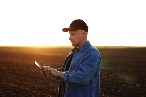 istock Smart farming technology and agriculture. Farmer uses digital tablet on field with plowed soil at sunset. Checking and control of soil quality, land readiness for sowing crops and planting vegetables 1578876556