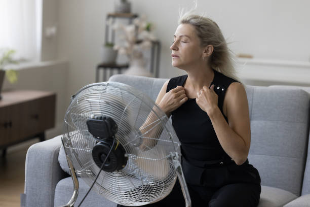 Sick exhausted woman sitting at fresh air blowing from propeller Sick exhausted senior woman with flying blonde hair and closed eyes hair sitting on couch at fresh air blowing from propeller, getting cool, refreshed at fan, feeling overheated, stress relief competition heat stock pictures, royalty-free photos & images