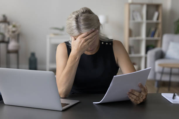 Depressed sad mature entrepreneur, business woman reading paper document stock photo