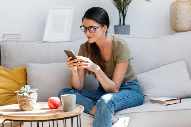 istock Beautiful woman using smartphone while relaxing in couch at home. 1578914605