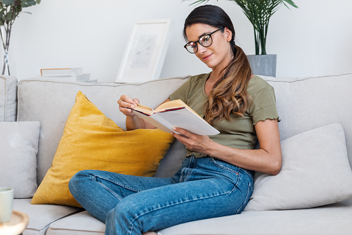 Shot of confident woman reading a book while sitting on sofa at home.