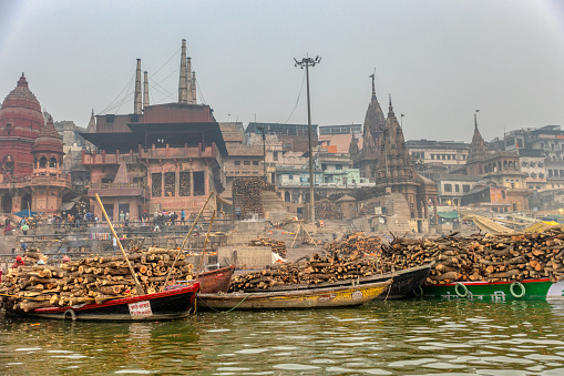 A wide-angle photograph of multiple boats on the Ganges river laden with firewood for the Manikarnika Ghat, one of the oldest cremation grounds in India's sacred city of Varanasi.