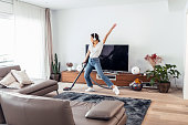 Young happy woman listening and dancing to music while cleaning the living room floor with a vaccum cleaner