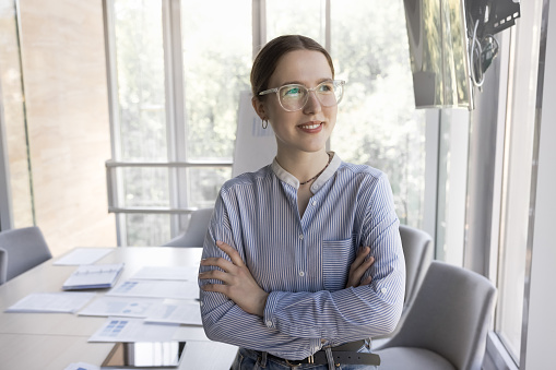 Happy dreamy business professional woman in glasses posing in office