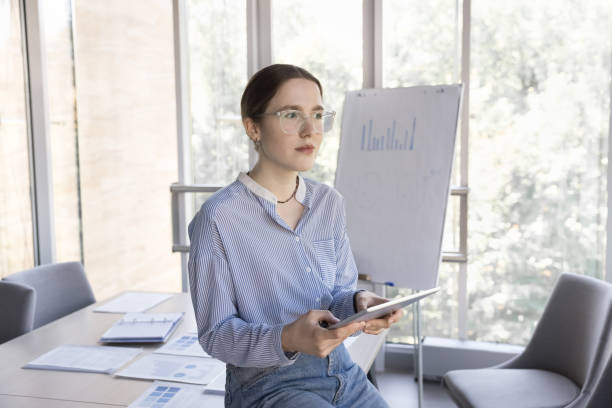 istock Thoughtful young business woman using digital tablet in office boardroom 1579039544